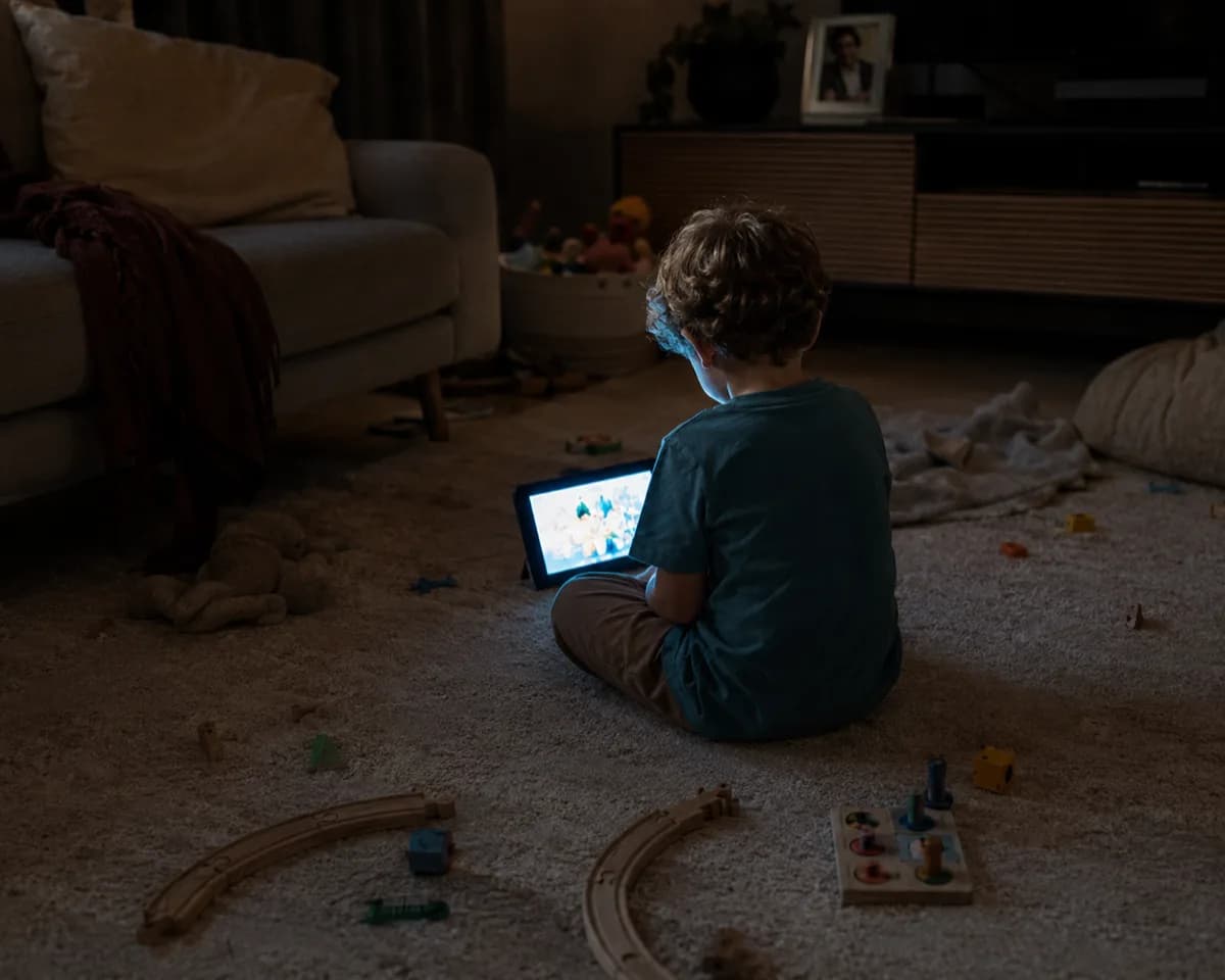 Criança sozinha no tapete escuro olhando um tablet